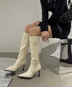 Close-up of cream white pointed toe knee-high boots with rivets and stiletto heels.