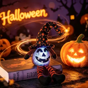 Glühende Halloween-Plüschkürbis-Puppe mit Hexenhut auf einem Buch sitzend dekoriert