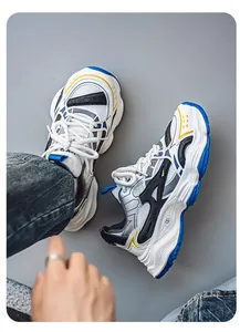 Top-down detail of white and blue retro chunky sneakers with yellow accents on grey floor.