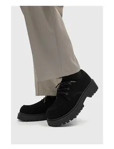 Primo piano di scarpe derby nere con suola alta abbinate a pantaloni grigi.