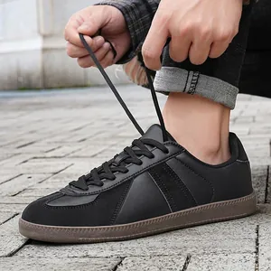 Casual men's black leather German Army Trainer sneakers shown being tied outdoors