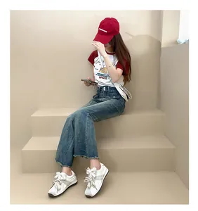 Detail view of stylish white suede sneakers with wide laces on a model sitting.