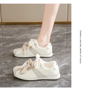 Close-up of stylish cream suede sneakers with elegant ribbon bow laces on marble floor.
