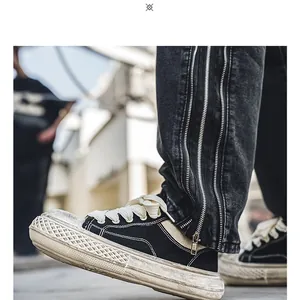Detalle de zapatillas de lona negra desgastada para hombre con suela gruesa y vaqueros con cremallera.