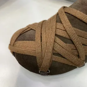 Κοντινό πλάνο καφέ σουέντ μοκασίνια με περίπλοκο σχέδιο χιαστί πλεχτών λουριών.