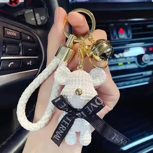 Macro view of a white textured bear keychain with a gold bell and decorative ribbon
