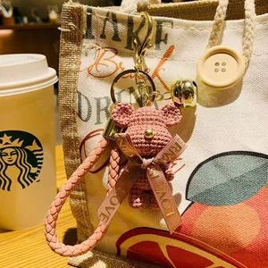 Close-up detail of a pink hand-knitted bear keychain accessory hanging on a rustic bag.