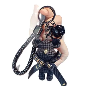 Elegant black knitted bear keychain with braided leather strap and gold ribbon