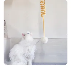Detailansicht einer weißen Katze, die mit einem gelben Feder- und Plüschballspielzeug spielt