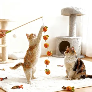 Primo piano di gatti che giocano con una bacchetta per gatti in legno con sei palline di peluche arancioni.