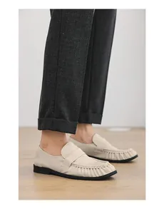 Close-up side view of cream leather loafers with pleated toe detailing and black soles.