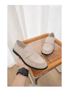 Close-up of beige croc-textured loafers with pleated toe design and black rubber sole