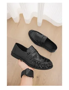Close-up of black designer slip-on loafers with textured pattern and pleated detail