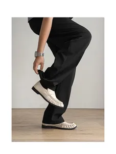 Close-up of off-white ruched leather loafers worn by a person wearing black trousers