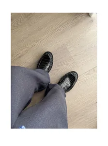 Close-up top-down view of black crocodile embossed loafers worn with grey trousers