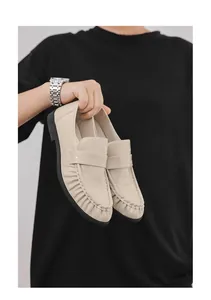 Detail shot of beige croc-embossed slip-on loafers held against black background