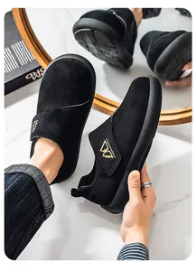 Detalle de mocasines de ante negro para hombre con correa de velcro y logo dorado.