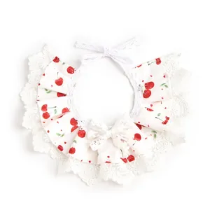 Primer plano de un babero blanco para mascotas con estampado de cerezas y lazo de encaje.