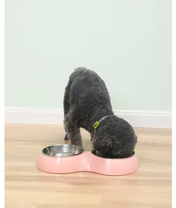 Grey poodle eating from a pink double stainless steel pet bowl on a wooden floor