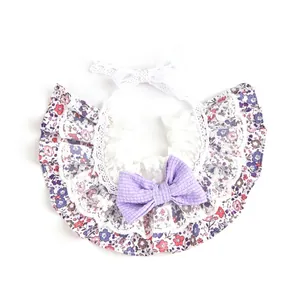 Vista detallada de un elegante babero para mascotas con flores, encaje blanco y lazo morado.