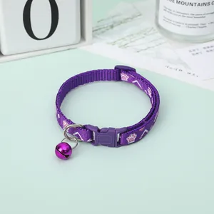 Detailed view of a purple cat collar with a bell and paw print pattern on green surface.