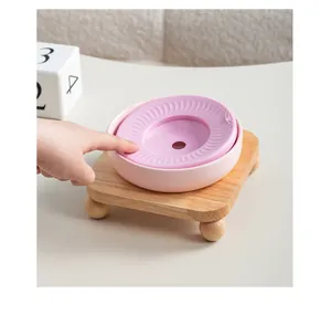 Gros plan d'une main pressant le disque flottant dans un bol en céramique rose sur bois