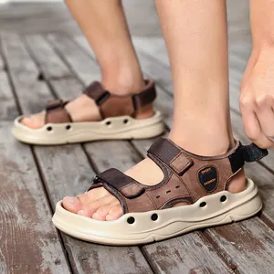 Sandali da spiaggia in pelle marrone da uomo con cinturini regolabili su legno.