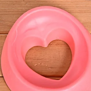 Dettaglio macro di un inserto per ciotola anti-ingozzamento rosa a forma di cuore su legno