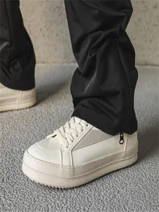 Détail de baskets compensées en cuir blanc et pantalon de jogging noir avec fermeture.