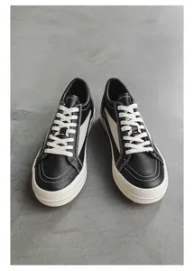 Vue de dessus de baskets en cuir noir avec lacets blancs sur sol texturé gris