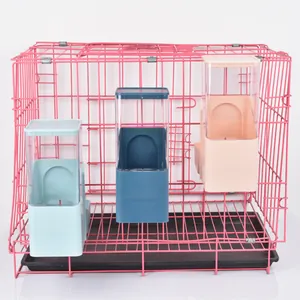 Detail of three hanging automatic pet feeders in blue and pink colors on a wire cage.