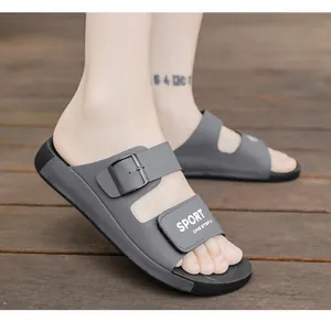Detailaufnahme grauer Herren-Sandalen mit Schnalle und SPORT-Schriftzug auf einem Holzdeck