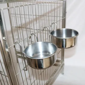 Stainless steel parrot feeder cups with hooks hanging on a metal bird cage frame