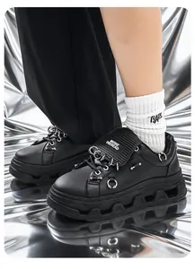 Dettaglio di sneaker con zeppa in pelle nera stile punk con accenti di anelli metallici.