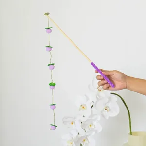 Mano che tiene una canna da pesca per gatti con palline di feltro viola e foglie verdi