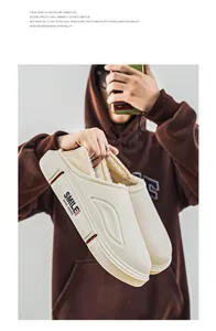 Detailansicht beige plüschgefütterte Hausschuhe gehalten von Person im braunen Hoodie