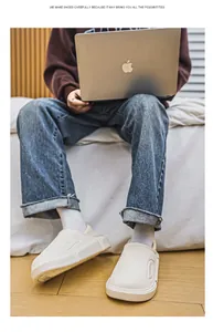 Ein Mann trägt weiße warme Winterhausschuhe während er im Bett am Laptop arbeitet