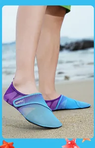 Dettaglio delle scarpe da scoglio in maglia sfumata viola e blu su una spiaggia sabbiosa.