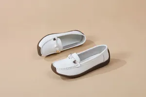 Detail shot of white women's loafers with brown soft soles and metal buckle detail.