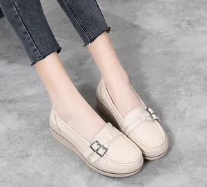Detailed close-up of beige wedge loafers with metal buckles and decorative stitching