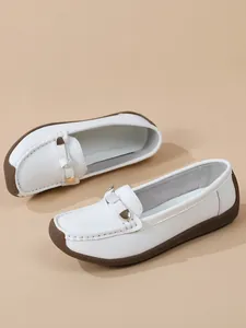 Close-up of white soft leather loafers with gold buckle detail and brown rubber sole.