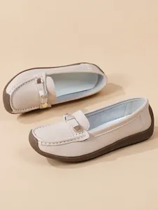 Close-up of beige leather loafers with textured soft sole and decorative metal buckle detail