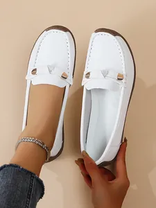 Close-up view of white soft-sole leather loafers featuring a decorative gold bow