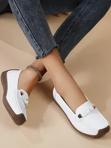 Close-up of white women's soft sole loafers worn with denim jeans and an anklet.