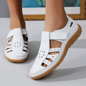 Gros plan de sandales plates en cuir blanc avec fleurs découpées au laser et semelle