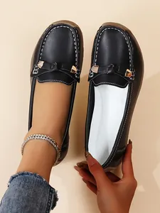 Close-up view of black slip-on loafers featuring white stitching and bow accent
