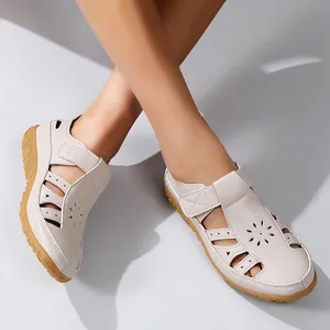 Gros plan de sandales plates beiges pour femmes avec détails de fleurs ajourées.