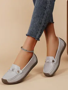 Close-up detail of grey leather loafers featuring white stitching and metal buckle accents