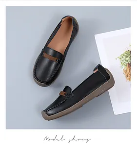 Elegante zwarte leren loafers met zachte zolen en decoratieve riempjes op grijze achtergrond.