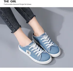 Close-up detail of stylish blue denim slip-on mules featuring white laces and frayed edges